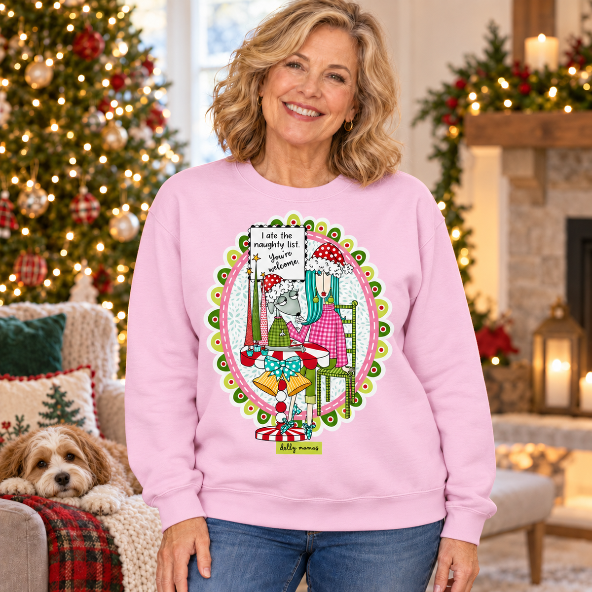 Woman wearing a pale lavender Dolly Mamas “I Ate the Naughty List. You’re Welcome” sweatshirt beside a Christmas tree, fireplace, and resting dog.