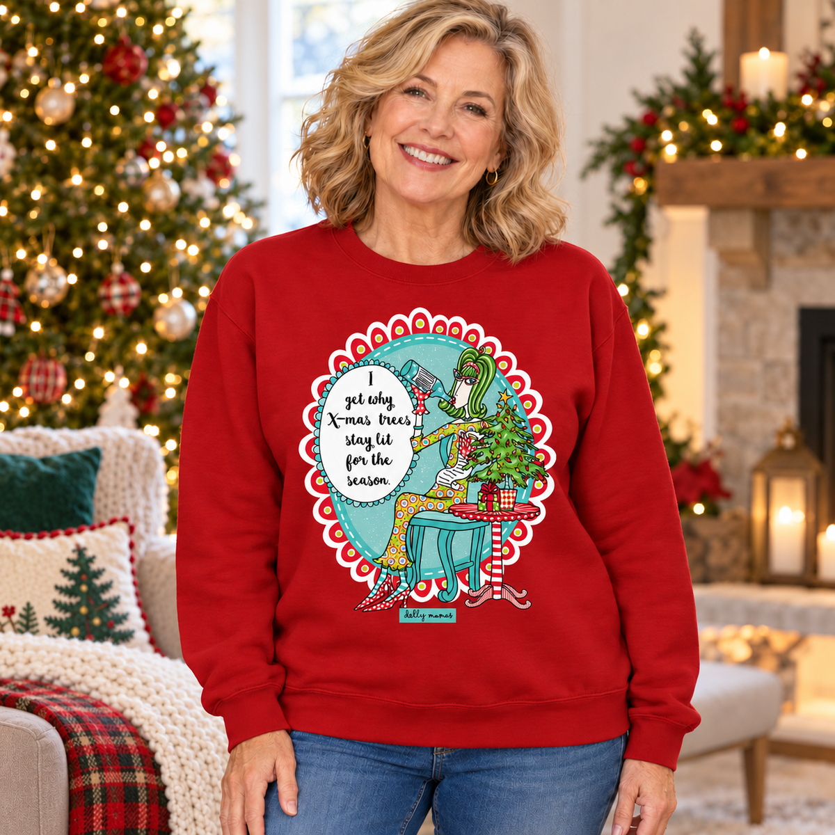 Woman wearing a cardinal red Dolly Mamas “I Get Why X-mas Trees Stay Lit for the Season” sweatshirt beside a Christmas tree and fireplace.