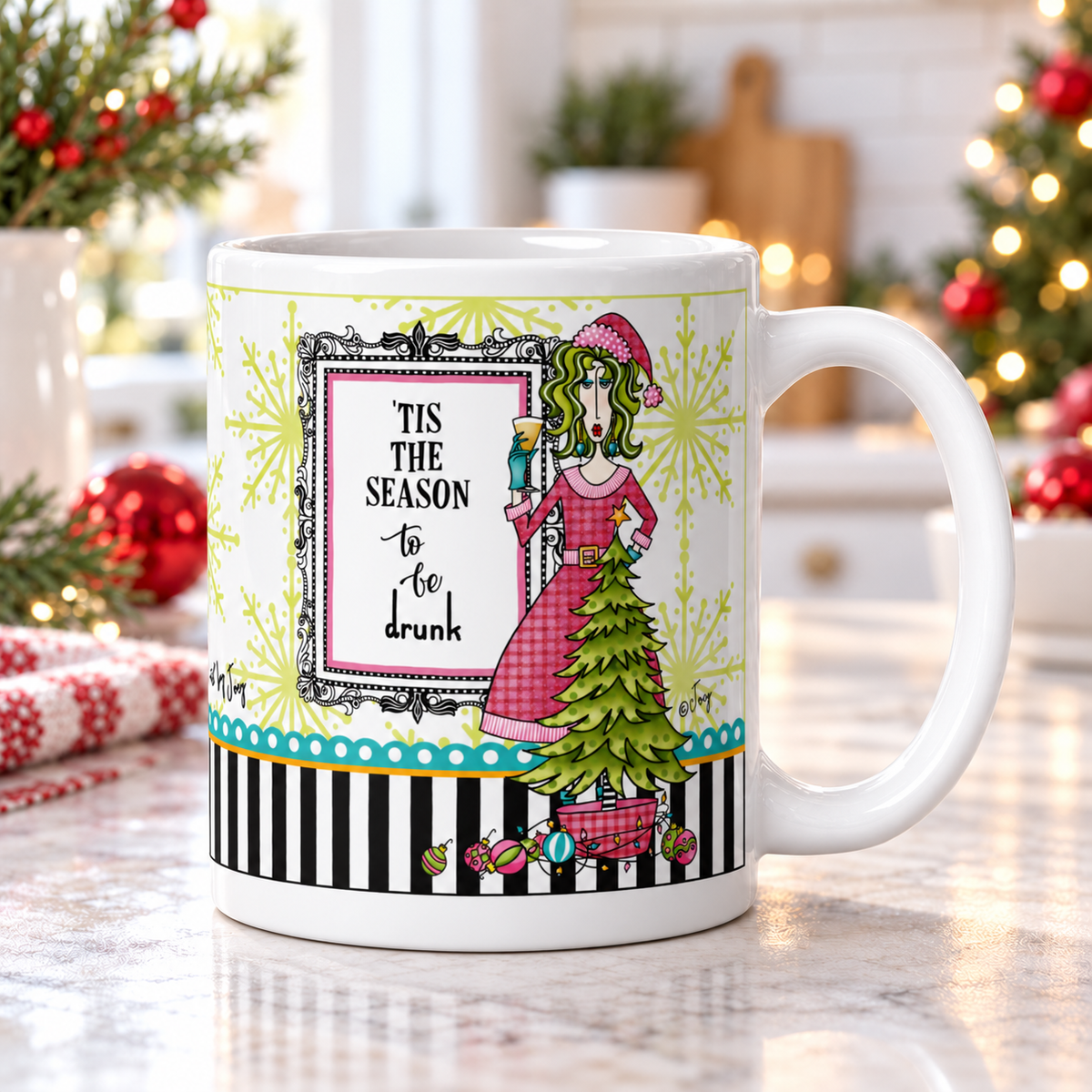 Dolly Mama “’Tis the Season to Be Drunk” mug on a bright kitchen counter, handle right, with Christmas greenery and red ornaments.