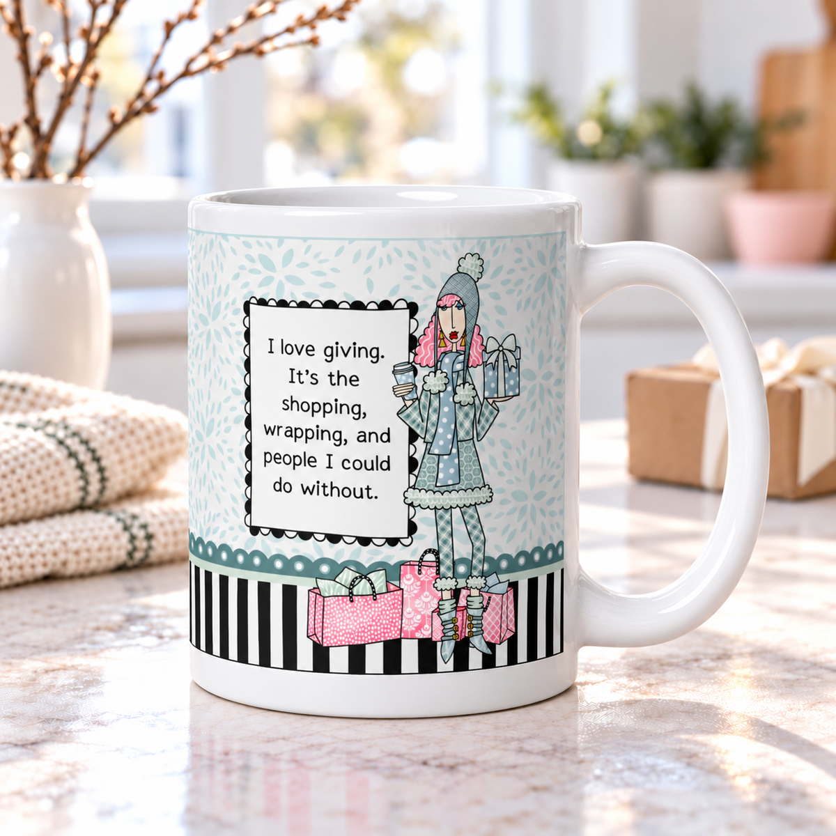 Dolly Mama “I Love Giving” holiday coffee mug on a bright kitchen counter, featuring a winter shopper with gifts and the quote “I love giving. It’s the shopping, wrapping, and people I could do without.”