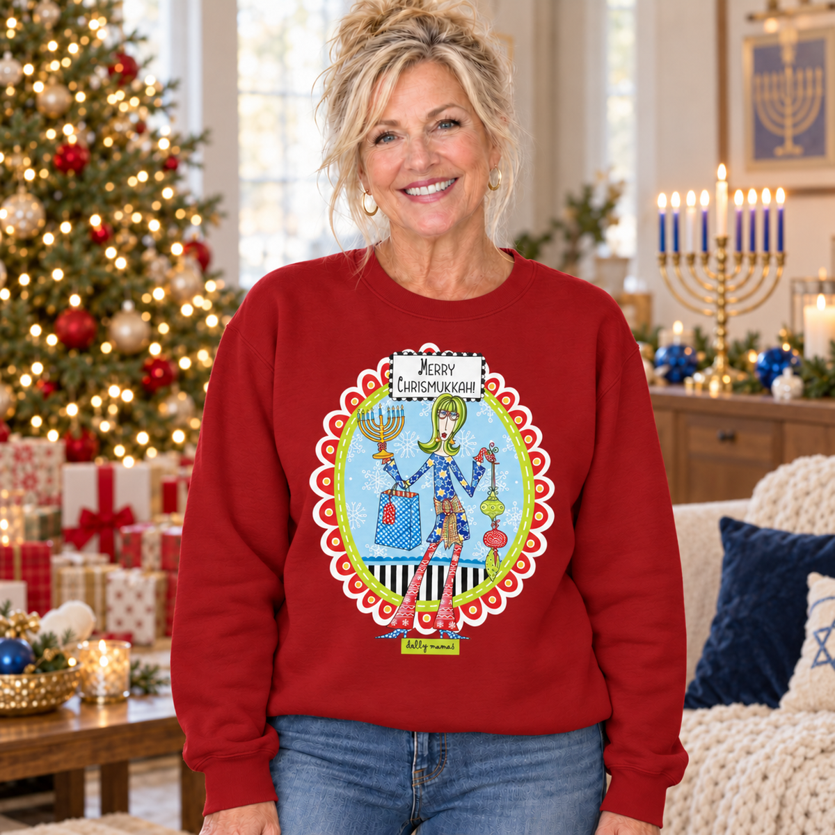 Woman wearing a cardinal red Dolly Mamas Merry Chrismukkah sweatshirt beside a decorated Christmas tree and lit menorah.
