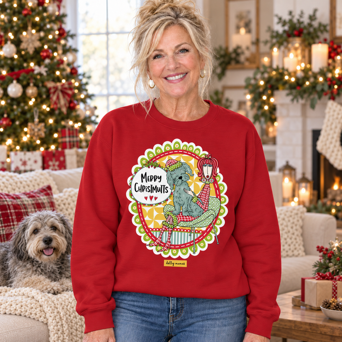 Woman wearing a cardinal red Dolly Mamas Merry Christmutts sweatshirt beside a shaggy dog in a room decorated for Christmas.
