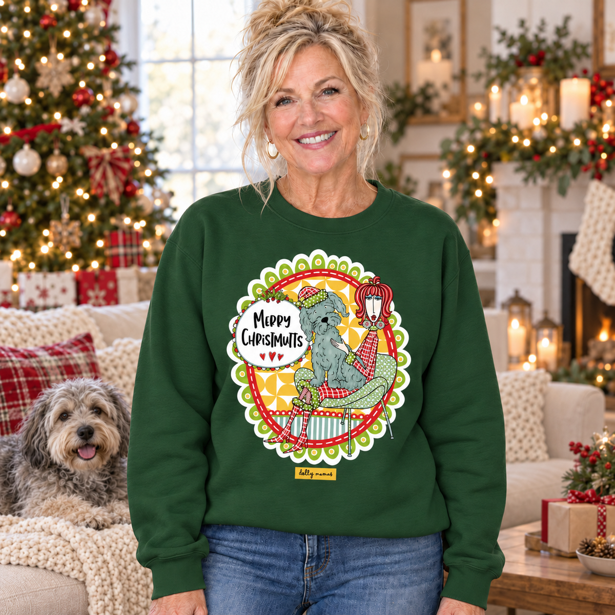 Woman wearing a forest green Dolly Mamas Merry Christmutts sweatshirt beside a shaggy dog in a room decorated for Christmas.
