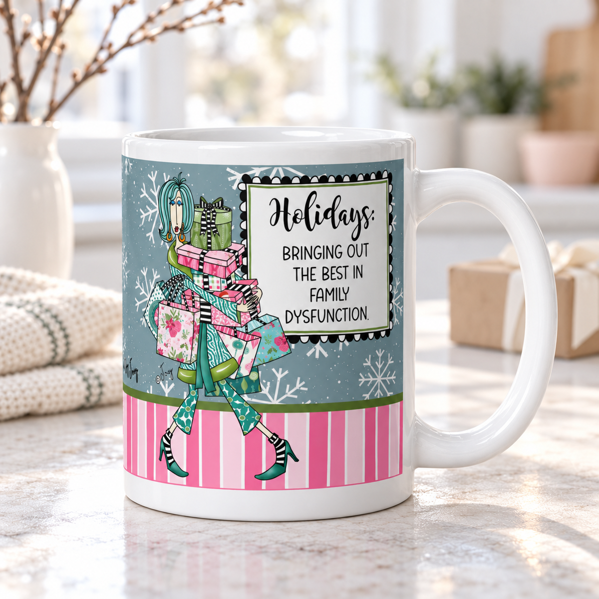 
Dolly Mama “Holidays: Bringing Out the Best in Family Dysfunction” mug on a kitchen counter, handle right, with wrapped gifts in the background.
