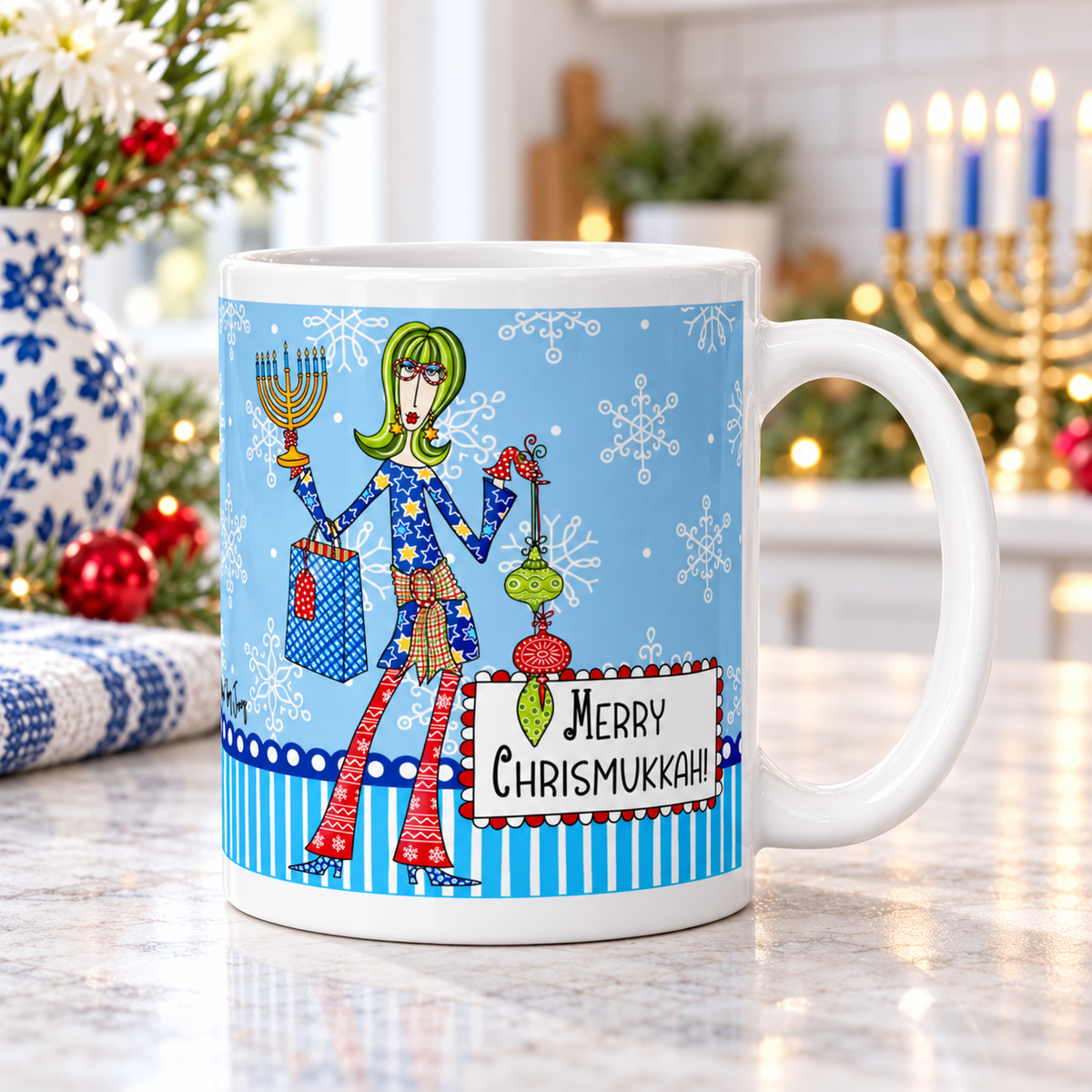 
Dolly Mama “Merry Chrismukkah!” mug on a bright kitchen counter, handle right, with Christmas greenery, red ornaments, and a menorah.
