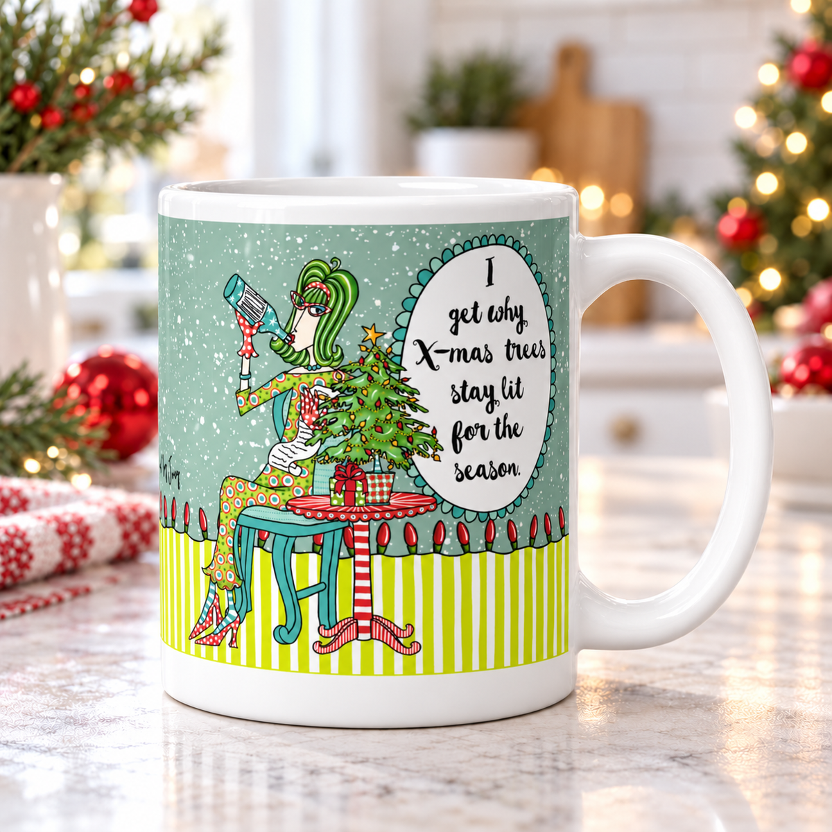 
Dolly Mama “I Get Why X-mas Trees Stay Lit for the Season” mug on a kitchen counter, handle right, with Christmas greenery and red ornaments.
